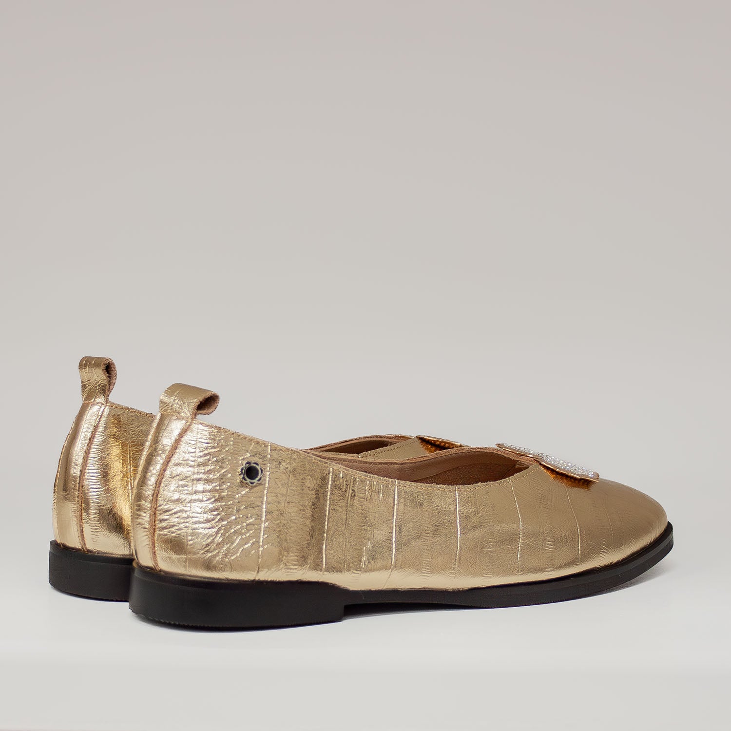 Złote baleriny Tuffoni z ozdobną pętelką z tyłu cholewki, na czarnej podeszwie, wykonane ze skóry naturalnej.