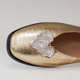 Zbliżenie na dekorację w kształcie serca wysadzaną cyrkoniami na złotej cholewce balerin Tuffoni ze skóry.