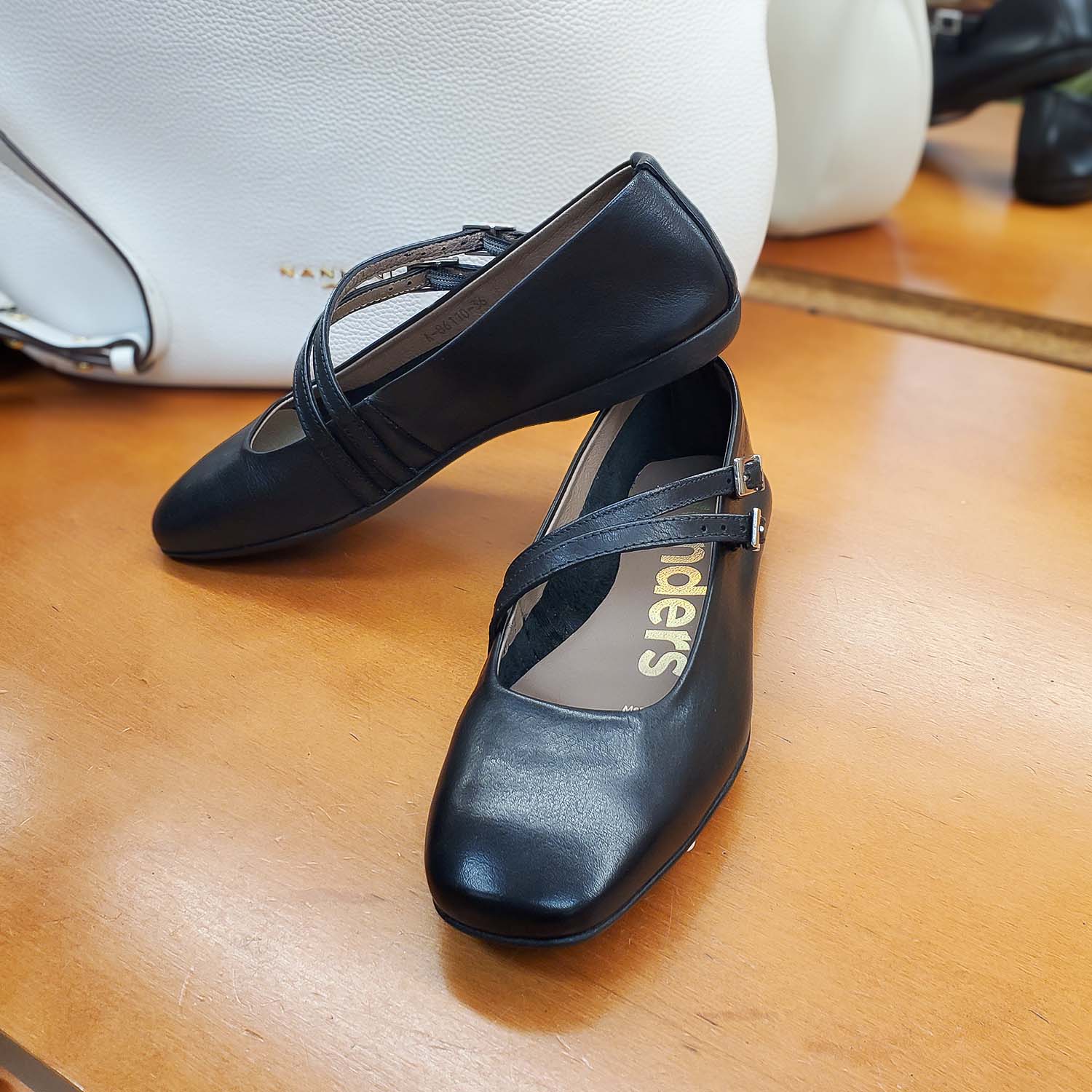 Baleriny Wonders – czarne, skórzane, Mary Jane widok w sklepie Buty i Kawa – czarne baleriny Mary Jane ustawione na ladzie, w tle biała torebka Nannini.
