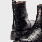 Botki Wonders – czarne, skórzane, lakierowane typu sztyblety z naturalnej skóry we wzór krokodyla, zbliżenie na nowoczesną fakturę skóry oraz detal logo na zapiętku.