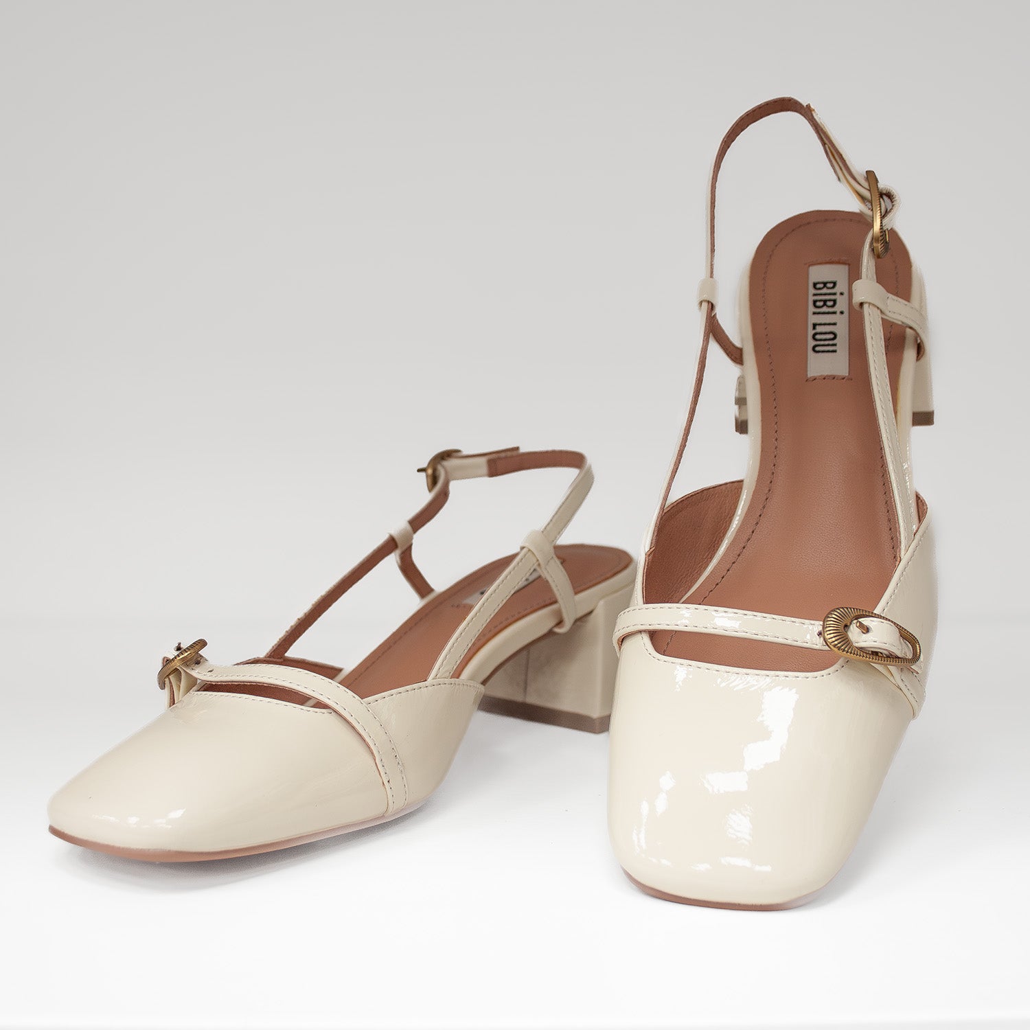 Hiszpańskie czółenka z odkrytą piętą Bibi Lou – kremowe, skórzane, lakierowane, widok z przodu eksponujące zdobne sprzączki.