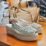 Espadryle Macarena na koturnie na wystawie sklepu obok plecionych torebek – letni klimat z espadrylami i dodatkami w naturalnych odcieniach beżu i słomy.