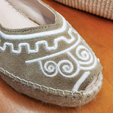 Zbliżenie na haft espadryli Macarena na koturnie – detal białego haftu na beżowej cholewce z miękkiego materiału, z wyraźnym obszyciem i widocznym noskiem.