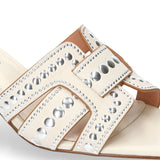 Zbliżenie na białe skórzane klapki Bibi Lou na słupku – detal cholewki z ozdobnymi wycięciami i srebrnymi nitami