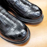 Czarne kozaki BONES od hiszpańskiej marki Wonders z naturalnej skóry licowej o wysokim połysku, tłoczonej w wyrazisty, zwierzęcy wzór na płaskiej podeszwie - zbliżenie na fakturę skóry.