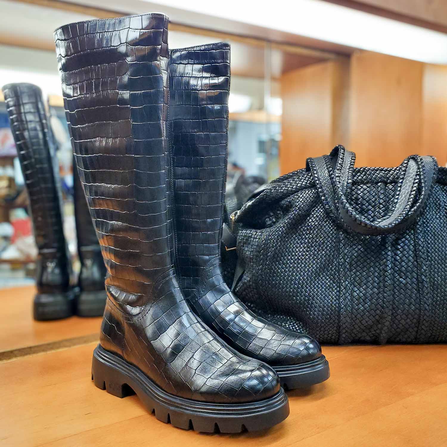 Czarne kozaki BONES od hiszpańskiej marki Wonders z naturalnej skóry licowej o wysokim połysku, tłoczonej w wyrazisty, zwierzęcy wzór na płaskiej podeszwie - widok z czarną torebką.