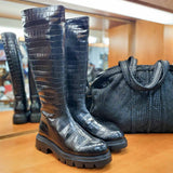 Czarne kozaki BONES od hiszpańskiej marki Wonders z naturalnej skóry licowej o wysokim połysku, tłoczonej w wyrazisty, zwierzęcy wzór na płaskiej podeszwie - widok z czarną torebką.