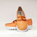 Mokasyny Wonders – pomarańczowe, skórzane, na platformie w ujęciu z przodu, z widoczną ozdobą w kolorze miedzi i tłoczeniem logo wewnątrz buta.
