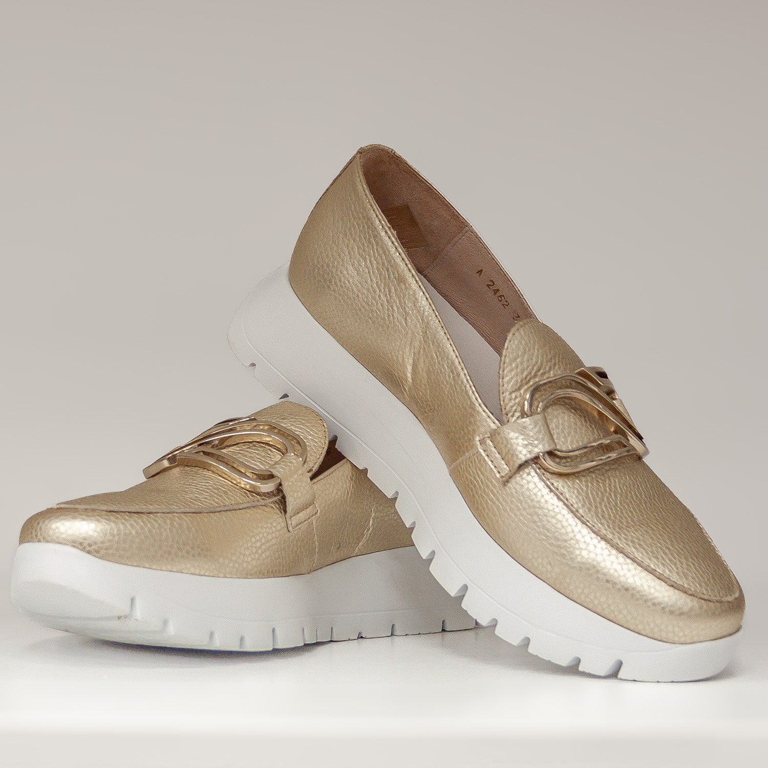 Złote mokasyny Wonders na białej platformie, sfotografowane w dynamicznej pozycji, eksponujące design i fakturę skóry.