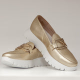 Złote mokasyny Wonders na białej platformie, sfotografowane w dynamicznej pozycji, eksponujące design i fakturę skóry.