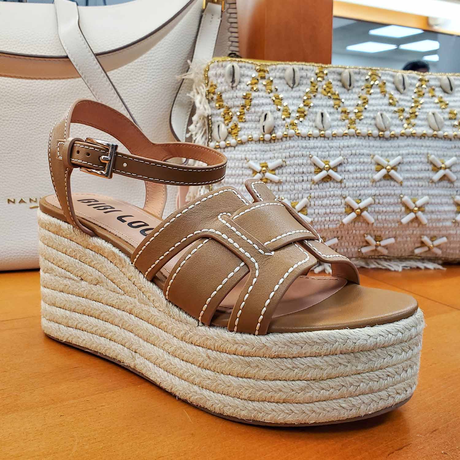 Sandały Bibi Lou brązowe skórzane na koturnie widok pod kątem – stylowe sandały z kontrastowym obszyciem, ustawione przy torebkach w letniej aranżacji.