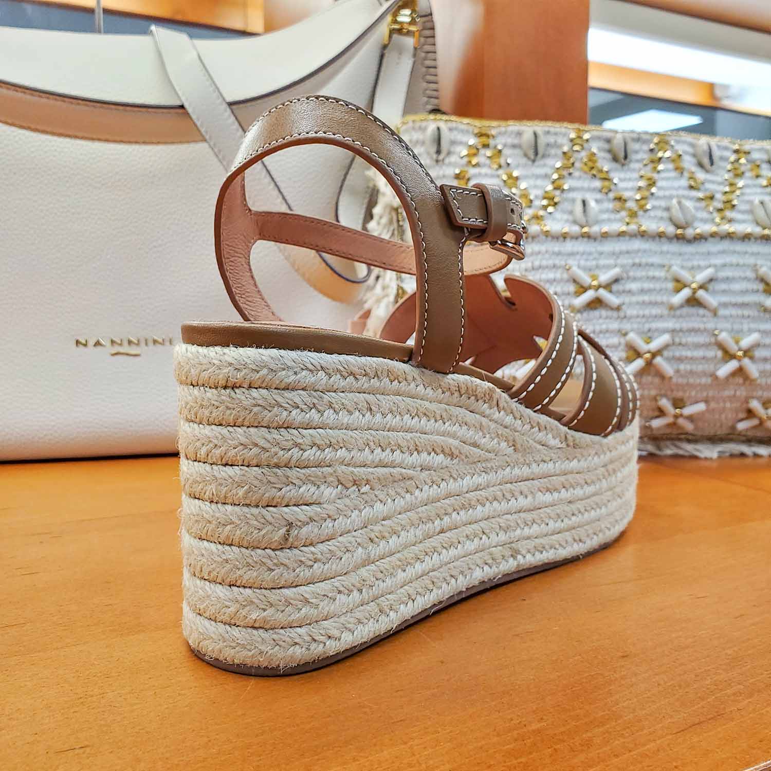 Sandały Bibi Lou brązowe skórzane na koturnie widok z tyłu – letnie sandały eksponujące pleciony koturn i pasek wokół pięty, zdjęcie na tle jasnych dodatków.