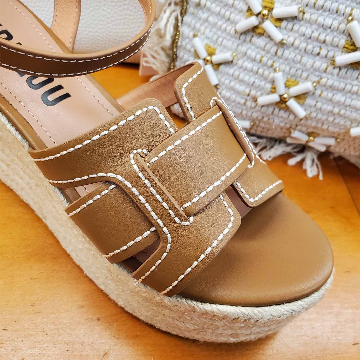 Sandały Bibi Lou brązowe skórzane na koturnie zbliżenie – detal cholewki z przeszyciami i sprzączką, pokazany na tle letnich akcesoriów.