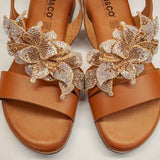 Zbliżenie na sandały Igi&Co – przestrzenna aplikacja z kryształków w kształcie kwiatów na tle naturalnej skóry licowej w ciepłym brązie.