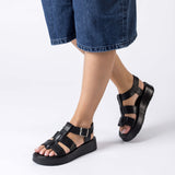 Sandały Wonders, czarne, skórzane, hiszpańskie na platformie – modelka prezentuje sandały na stopach, widoczna wysokość podeszwy i dopasowanie pasków.