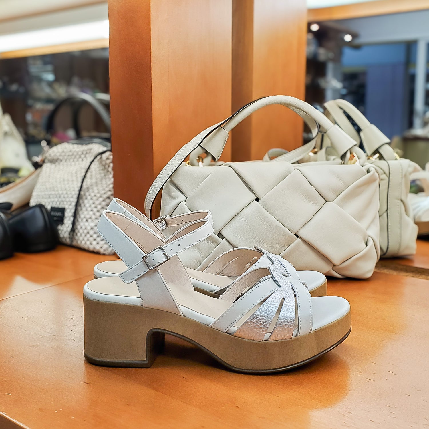 Sandały Drewniaki Wonders na półce w butiku Buty i Kawa, na tle kremowych torebek, pokazujące połączenie klasy i komfortu.