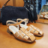 Para pomarańczowych sandałów na niskim obcasie Wonders ustawiona na sklepowej półce, z widoczną strukturą lakierowanej skóry i czarną torebką w tle.