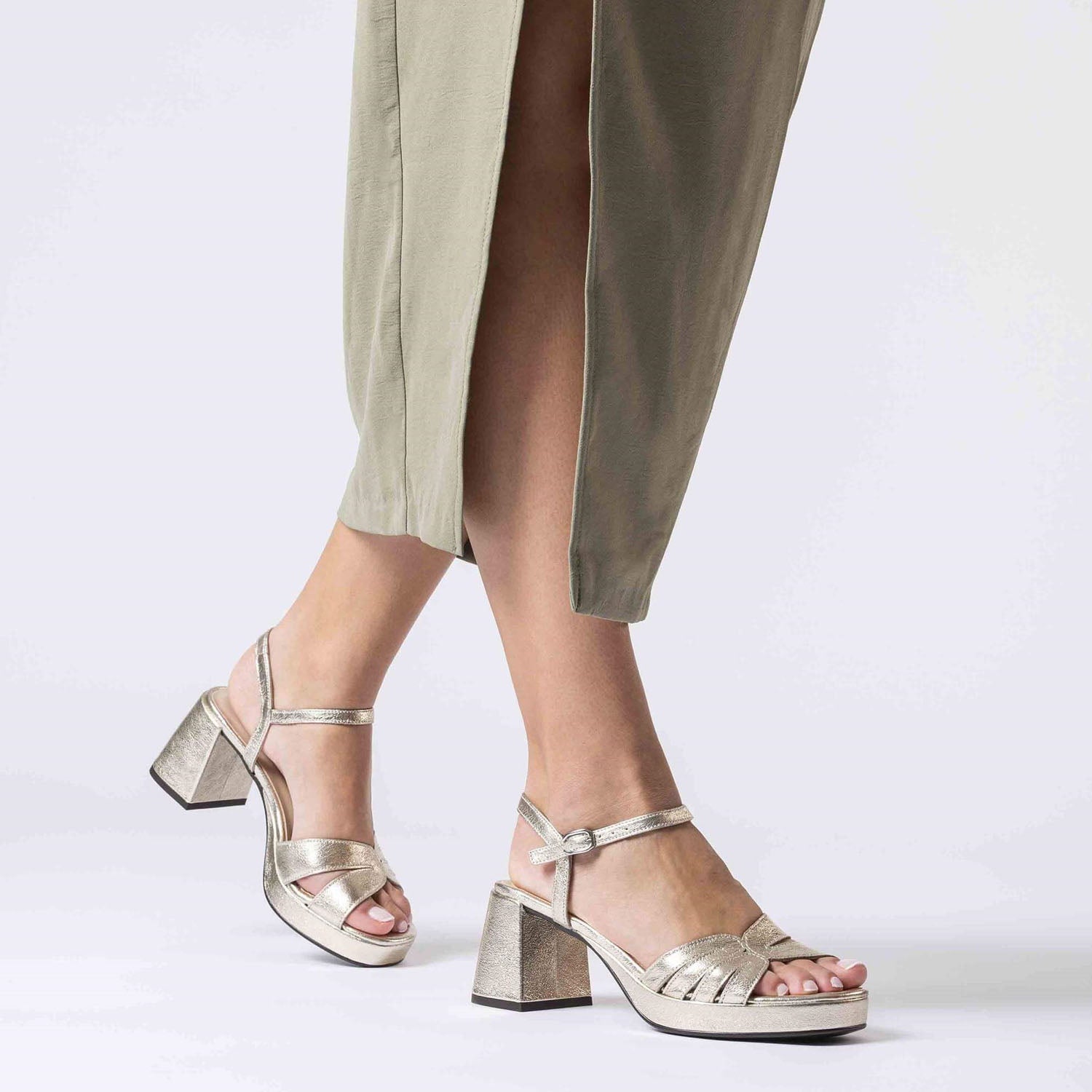 Modelka w beżowej sukience prezentuje złote sandały Wonders z naturalnej skóry, na wysokim słupku i platformie, w ujęciu w ruchu.