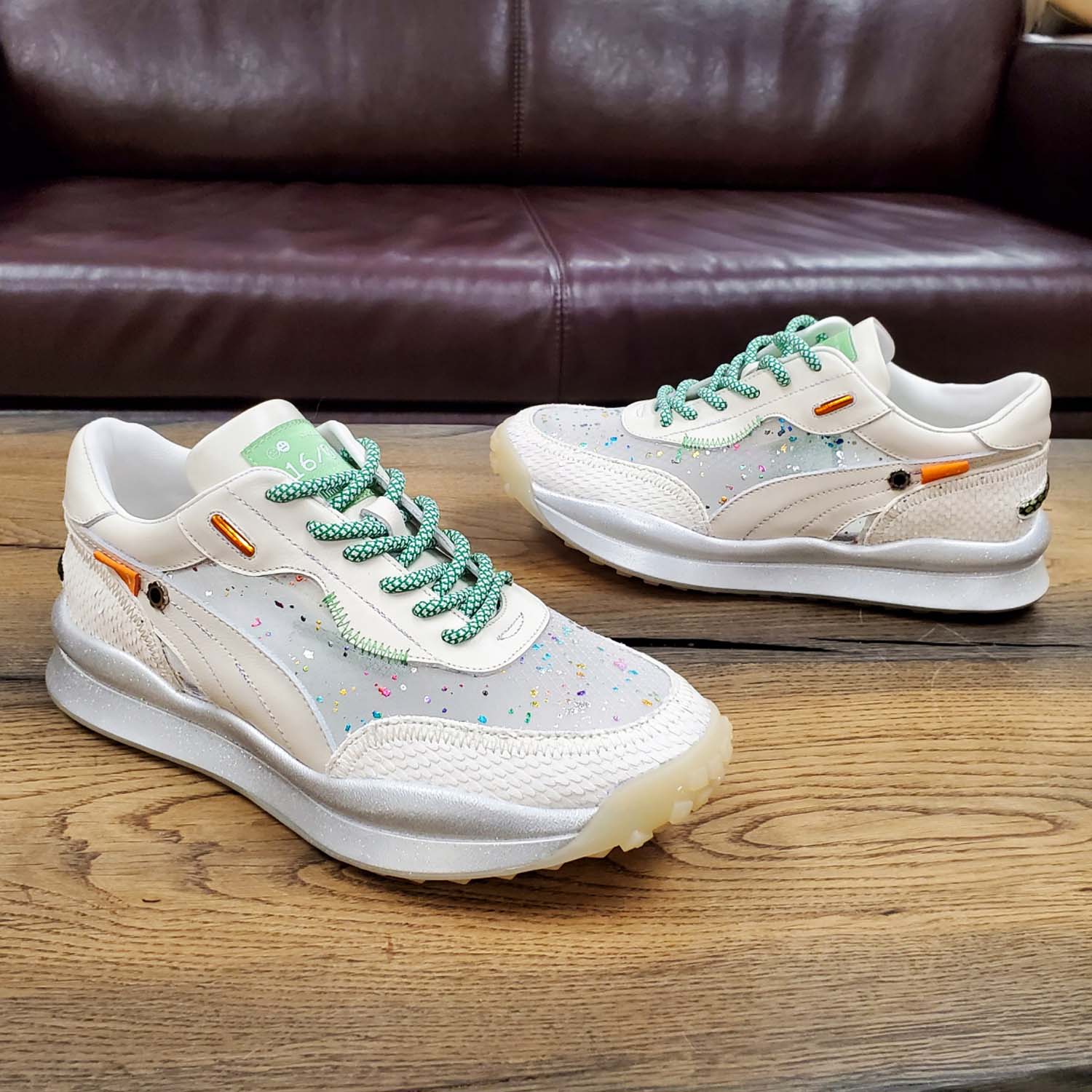 Sneakersy Tuffoni – ecru, z siateczką, skórzane, ujęcie na drewnianym blacie, widoczna transparentna cholewka z kolorowymi akcentami i kontrastowe sznurówki.