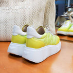 Sneakersy Wonders – limonkowe, skórzane, na platformie – widok od tyłu, para ustawiona na drewnianym blacie, w tle torba z plecionki