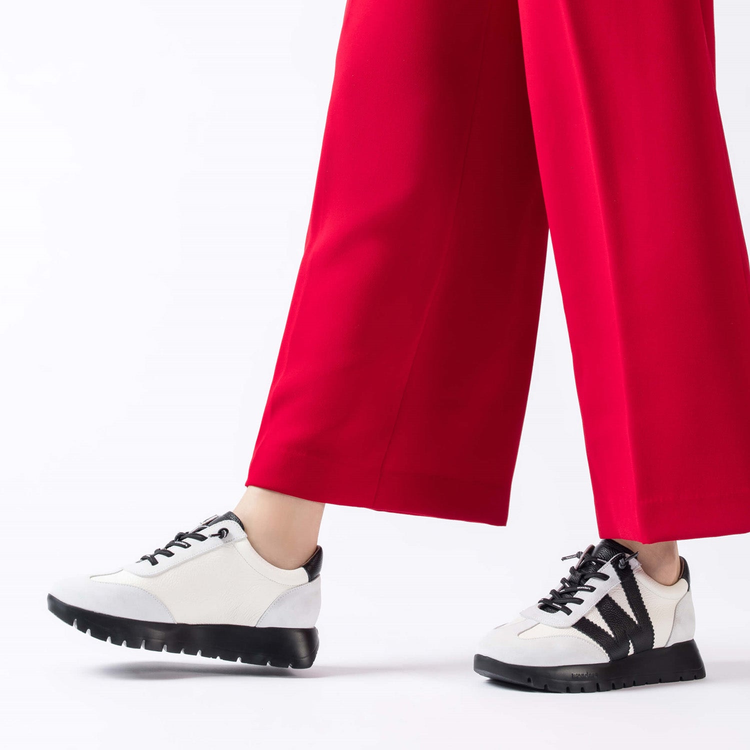 Hiszpańskie sneakersy Wonders – biało-czarne, skórzane, eleganckie z nowe jkolekcji 2025/2026 jesień/zima ze skóry naturalnej licowej i zamszowej, stylizacja na modelce z czerwonymi spodniami.