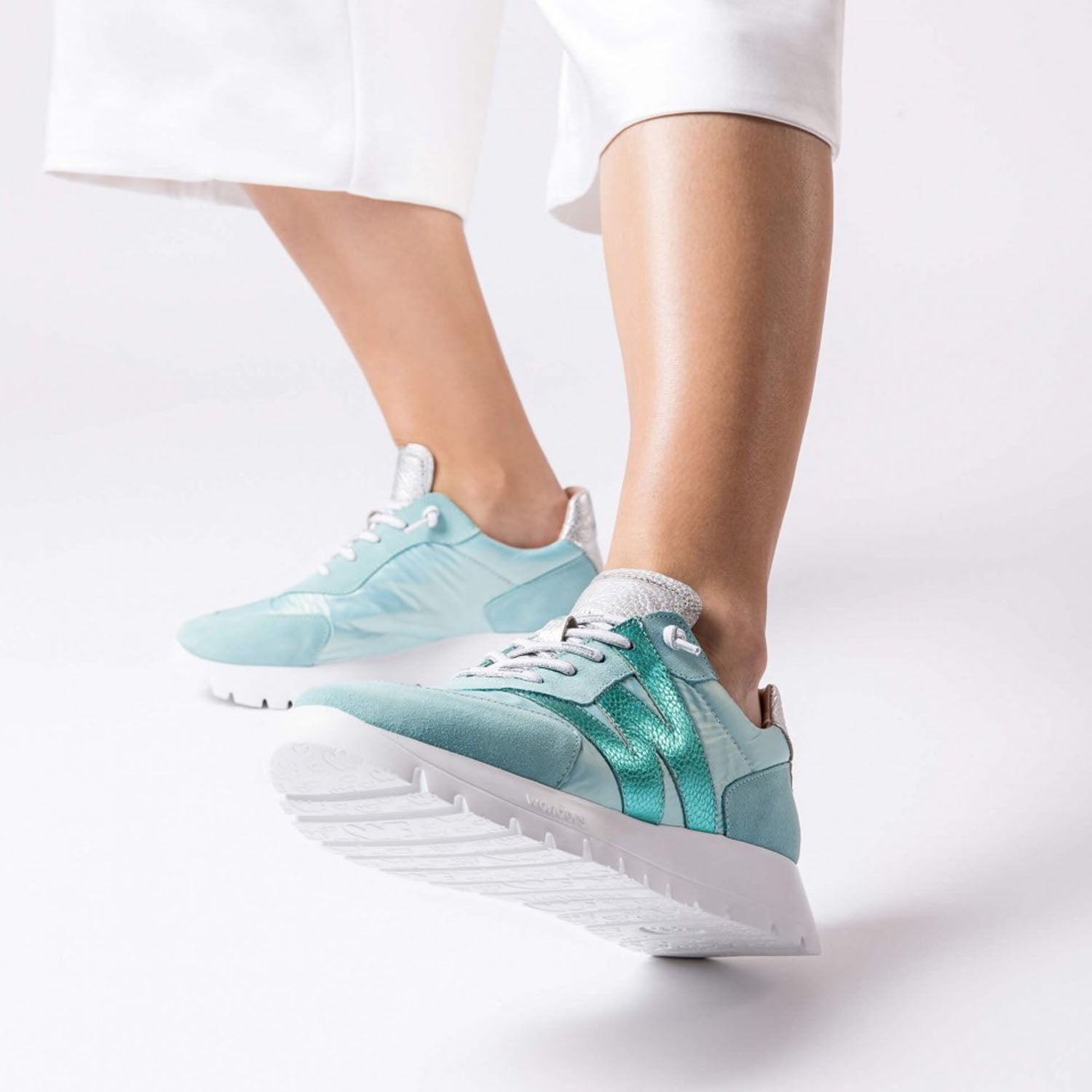 Sneakersy Wonders w kolorze mięty i turkusu założone przez modelkę, stylizacja z białymi spodniami i sportowym luzem.