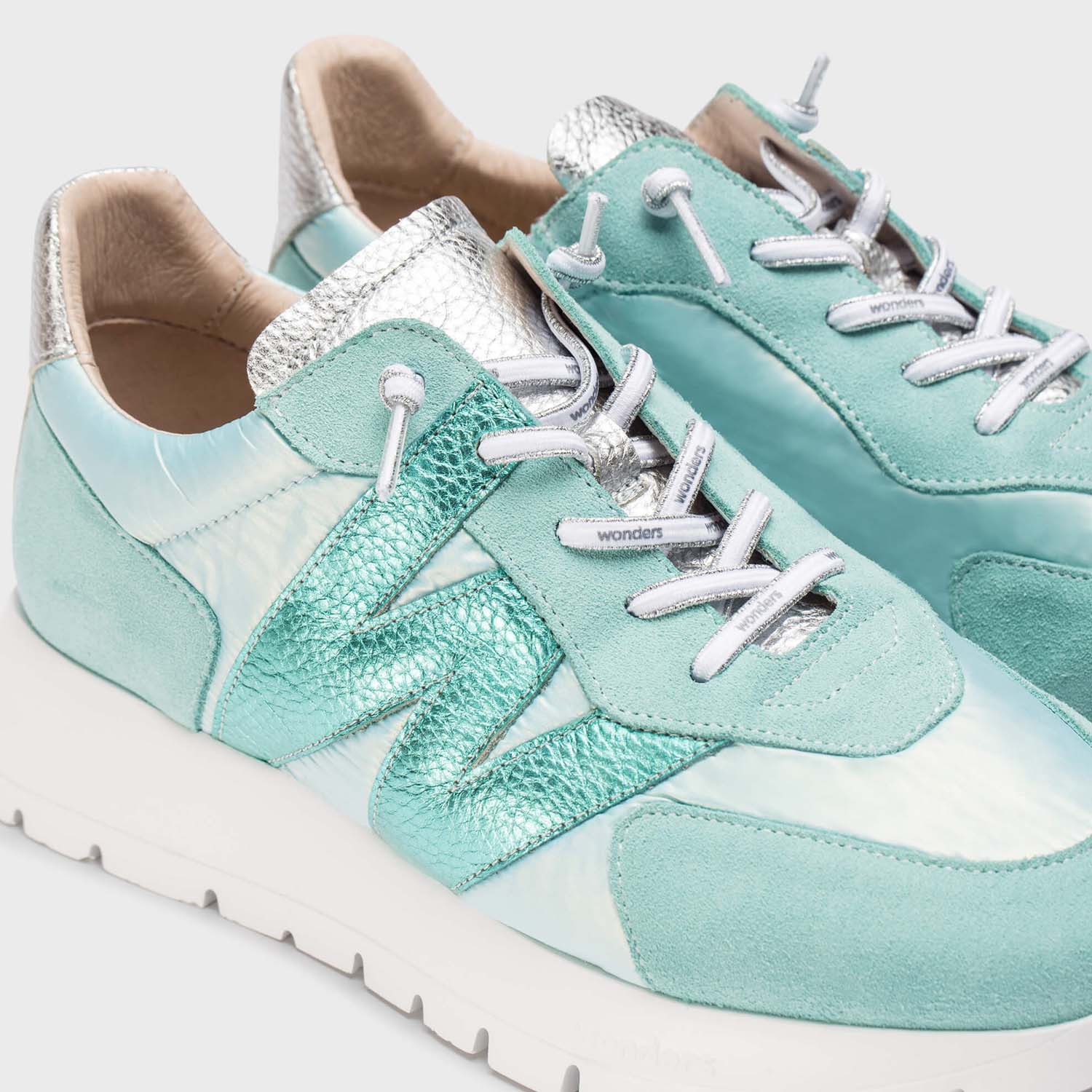 Zbliżenie na miętowe i turkusowe sneakersy Wonders z połyskiem, pokazujące fakturę skóry i srebrne wykończenia.