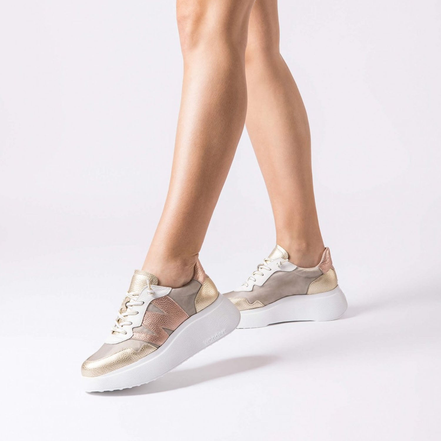 Sneakersy Wonders – złote, skórzane, na platformie prezentowane na stopach modelki w ruchu, z podkreśleniem wysokiej podeszwy.