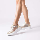 Sneakersy Wonders – złote, skórzane, na platformie prezentowane na stopach modelki w ruchu, z podkreśleniem wysokiej podeszwy.