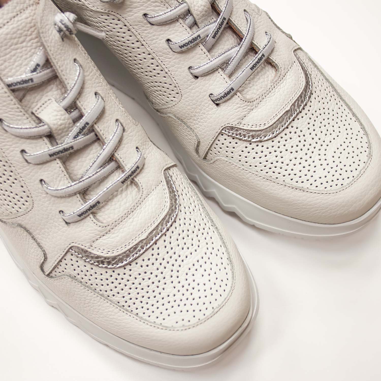 Zbliżenie na białe sneakersy Wonders z perforowaną fakturą i srebrnymi sznurówkami, ujęcie z góry pokazujące detaliczne wykończenie cholewki.