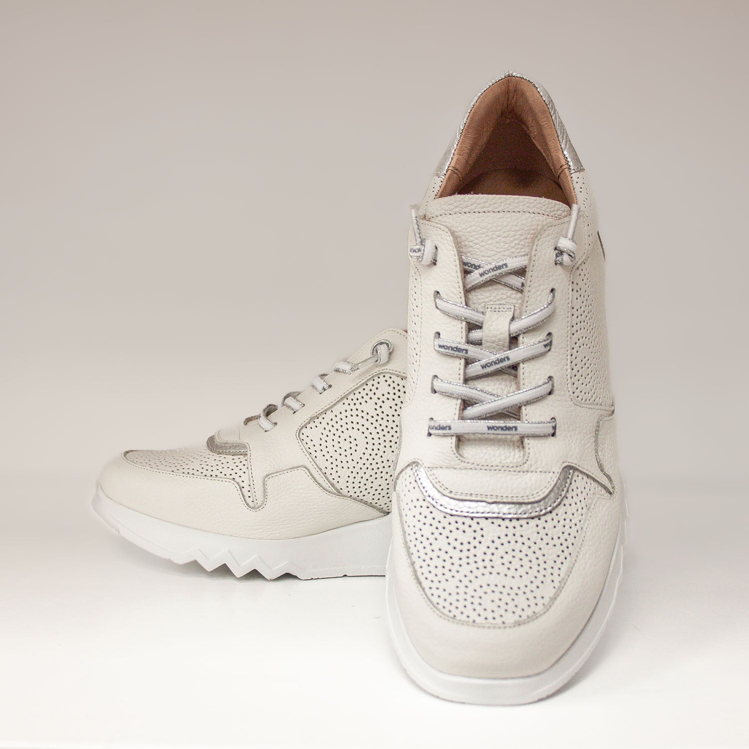 Białe sneakersy damskie Wonders z okrągłymi noskami i ażurowym wzorem, sfotografowane od frontu, ukazujące symetrię i sportowy charakter.