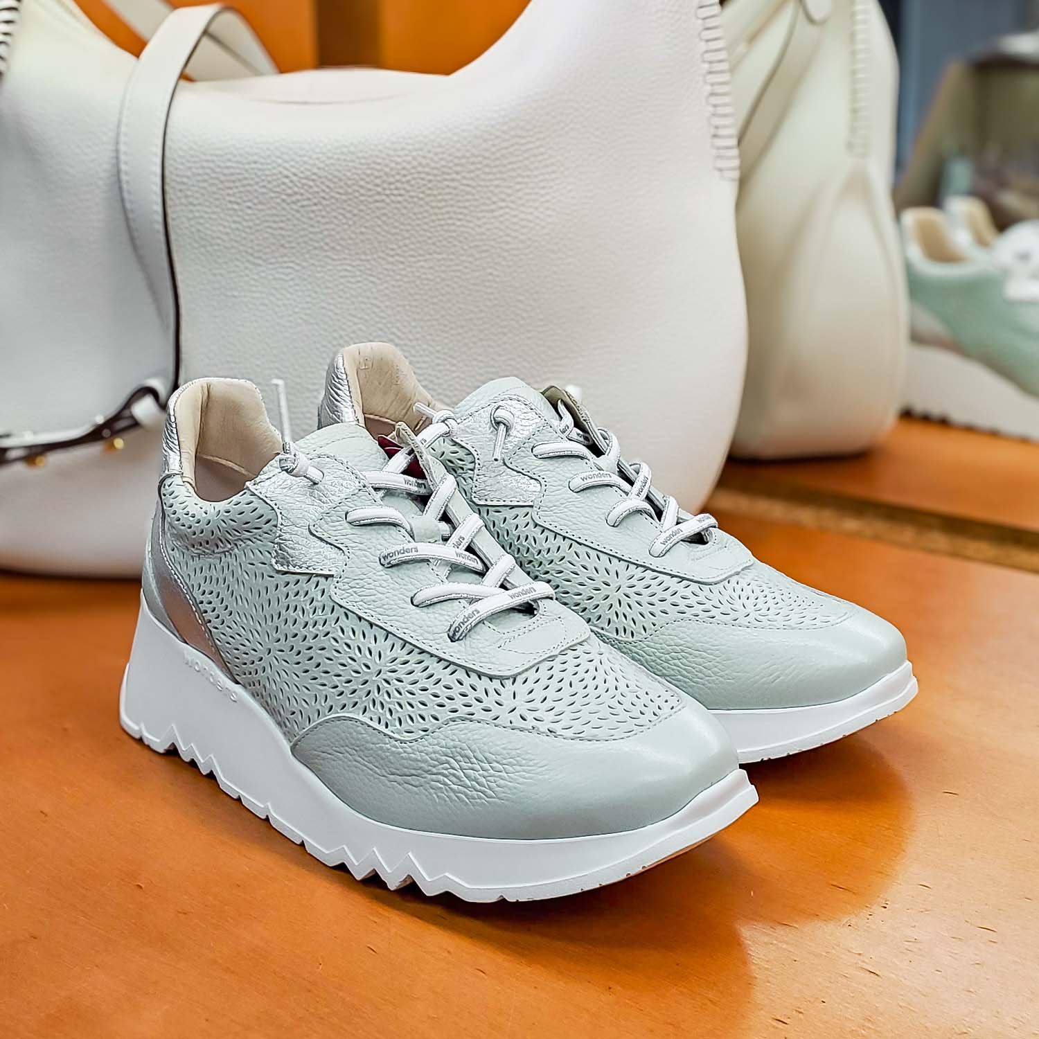 Skórzane sneakersy Wonders w odcieniu aqua z perforowaną cholewką i srebrnymi akcentami, ustawione na tle białej torby.