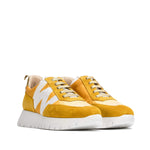 Sneakersy w ciepłym odcieniu żółci, z kontrastową białą podeszwą i ozdobnymi przeszyciami, widoczne pod lekkim kątem.