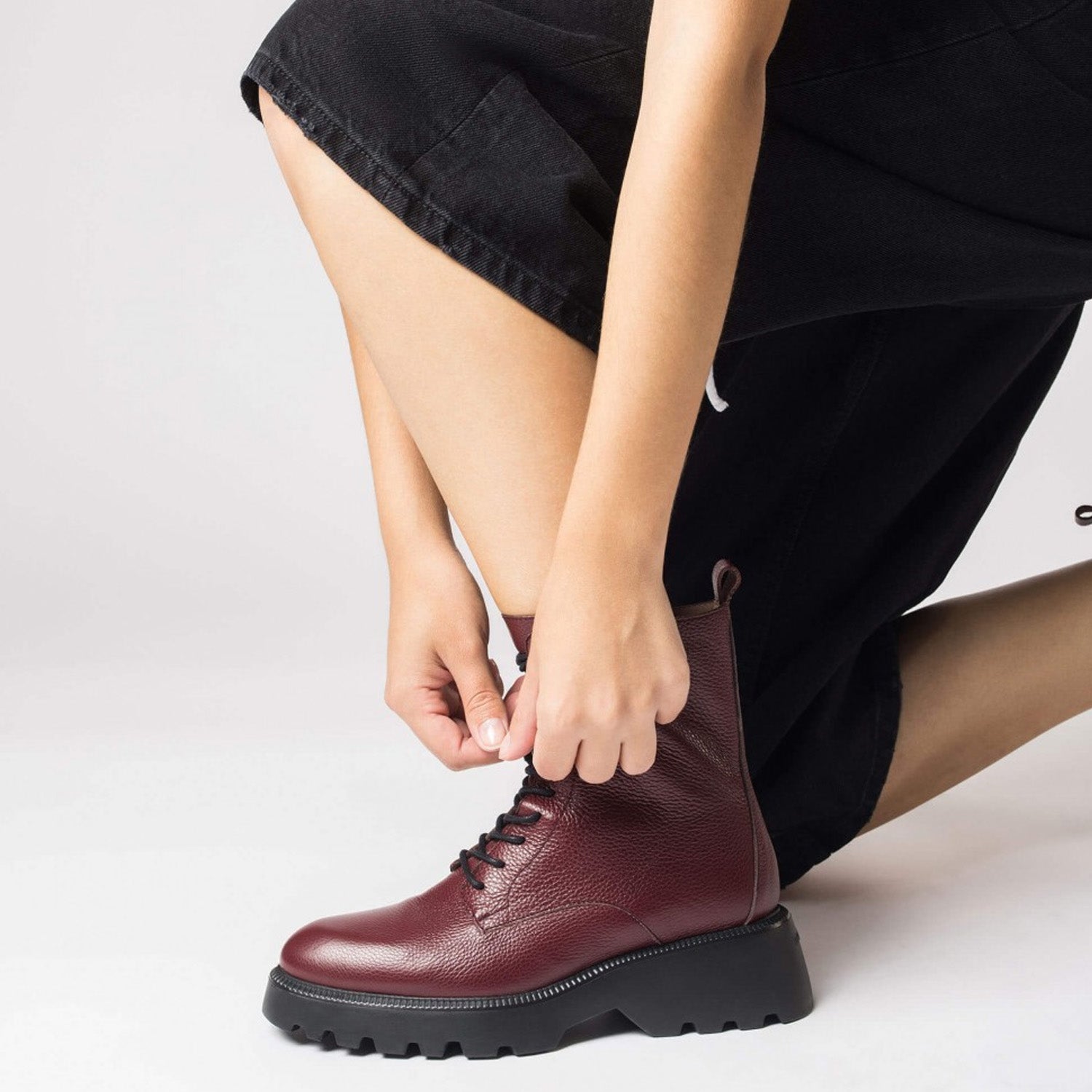 Bordowe botki Wonders w stylizacji – modelka zapina buty na suwak.